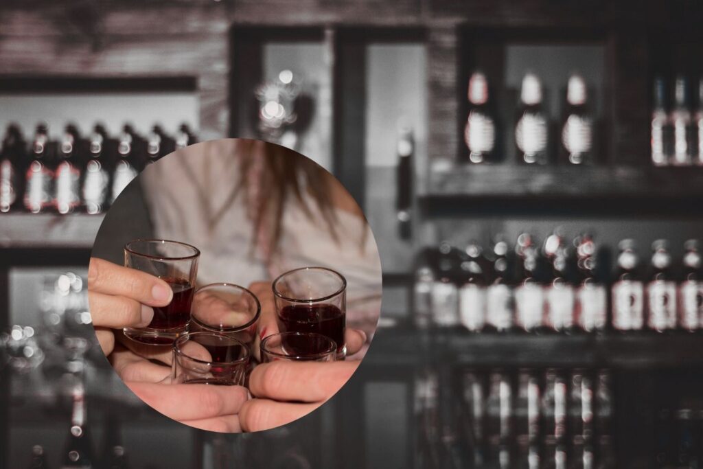 Anstoßen mit Shotgläsern vor Spirituosenregal