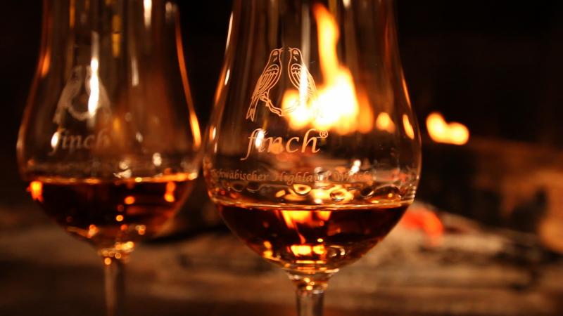 Whiskyglas mit Fin(ch)-Logo vor Kaminfeuer